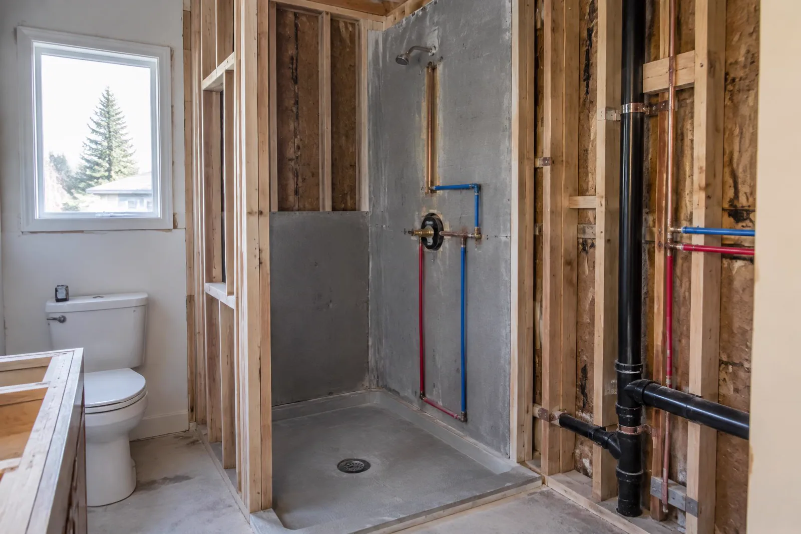 Bathroom remodel rough-in showing shower valve, supply lines, and drain plumbing before fixtures are installed